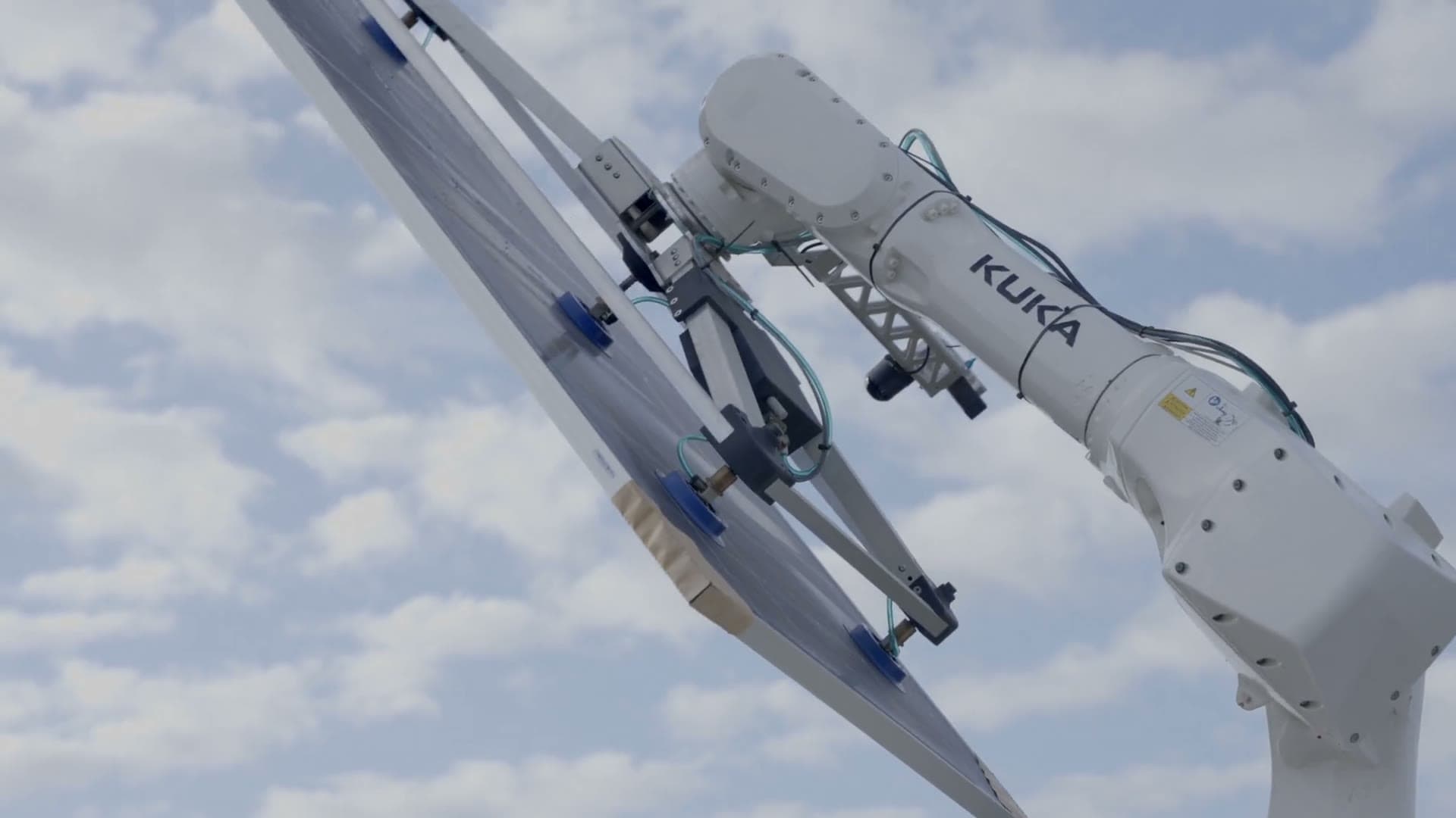 Cosmic-1 robotic arm lifting a solar panel against a cloudy sky in Southern Texas